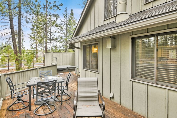 A covered patio with a table and chairs, a cushioned lounge chair, and a wooden deck.