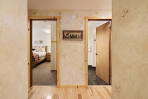 A hallway with wooden doors leading to a bedroom with a bed, a nightstand, and a wall-mounted picture. - Pine Needle 2 - A/C, Hot Tub, SHARC (Sunriver)