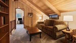 A cozy living room with a wooden ceiling, a sofa, a coffee table, a bookshelf, and a painting on the wall.