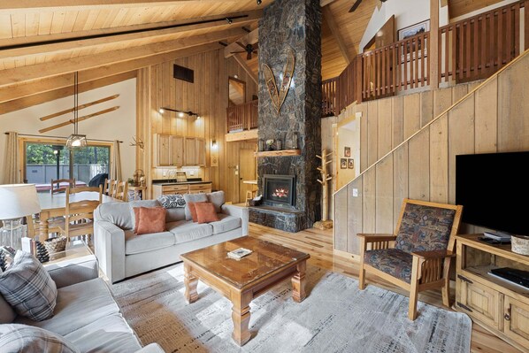 A spacious living area with a fireplace, wooden furniture, and a television. - Pine Needle 2 - A/C, Hot Tub, SHARC (Sunriver)