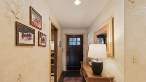 A hallway with framed pictures on the walls, a wooden console table with a lamp, and a door at the end.