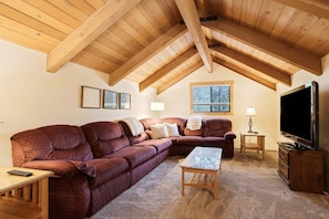 A cozy living room with a large sectional sofa, a coffee table, a television, and a window with blinds. - Pine Needle 2 - A/C, Hot Tub, SHARC (Sunriver)