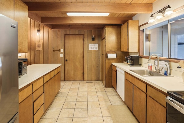 A compact kitchen with wooden cabinets, a built-in dishwasher, a microwave, and a sink with a window above. - Pine Needle 2 - A/C, Hot Tub, SHARC (Sunriver)