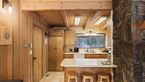 A kitchen with wooden cabinets, a large window, and a stone wall.