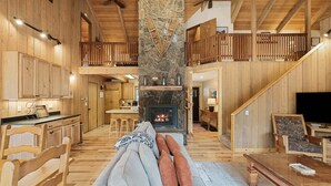 A spacious living area with a fireplace, wooden furniture, and a high ceiling with exposed beams.