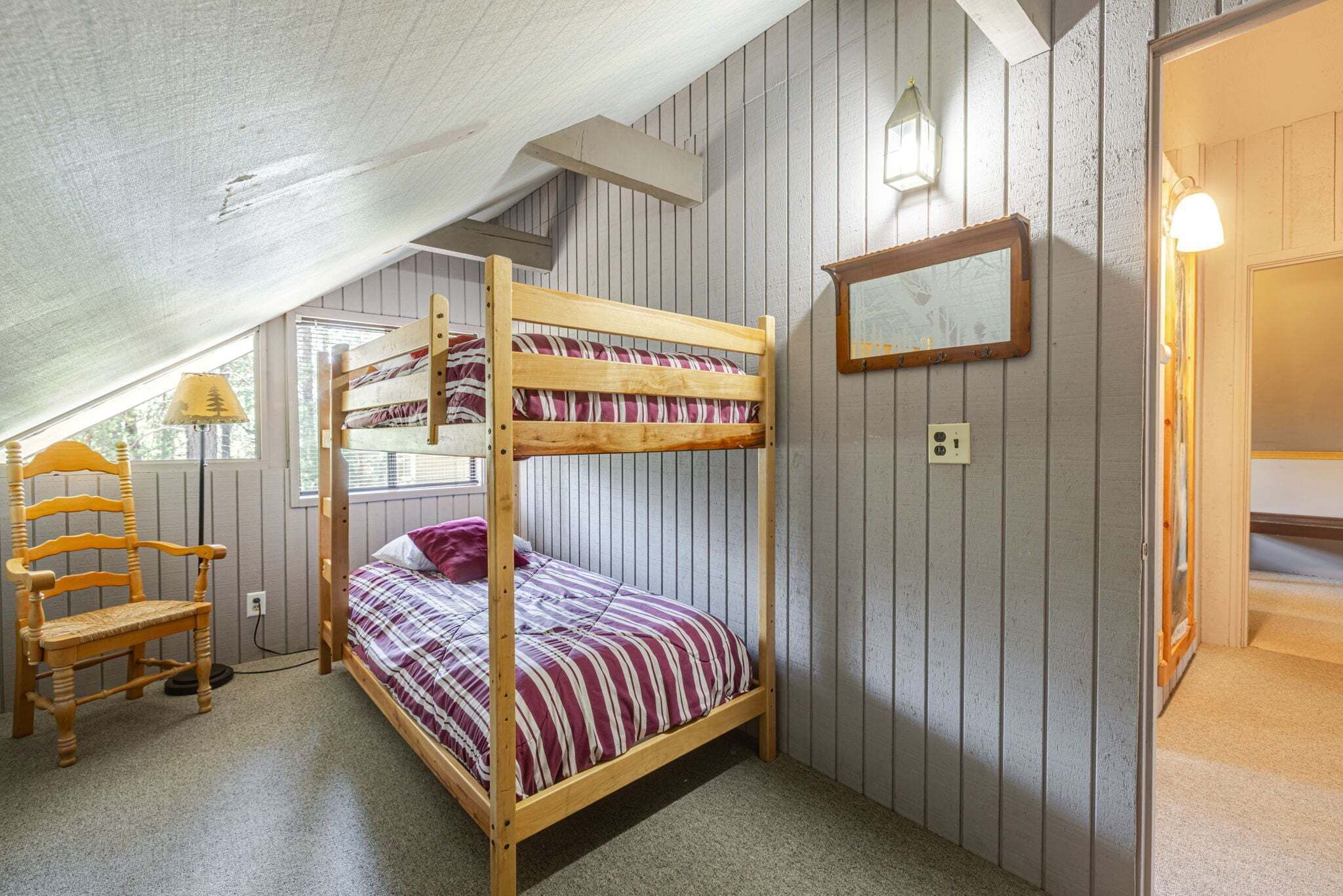 A bunk bed room with a wooden chair, a window, and a wall-mounted light fixture.