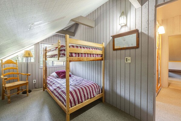 A bunk bed room with a wooden chair, a window, and a wall-mounted light fixture.