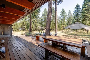A wooden deck with picnic tables and benches, surrounded by tall pine trees.