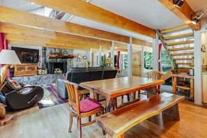 A spacious living area with a large wooden table, comfortable seating, a fireplace, and a staircase leading to an upper level.