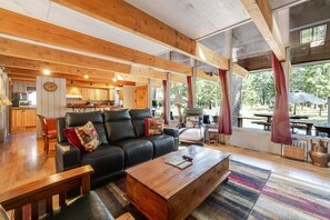A spacious living area with a black leather sofa, wooden coffee table, and a view of the kitchen and outdoor patio.