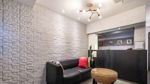 A modern lobby with a textured white wall, a black leather sofa with red cushions, and a woven side table. - Mac Hotel (Seoul)