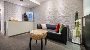 A modern reception area with a stone-textured wall, a black leather sofa with colorful cushions, a glass coffee table, and a kitchen counter with appliances. - Mac Hotel (Seoul)