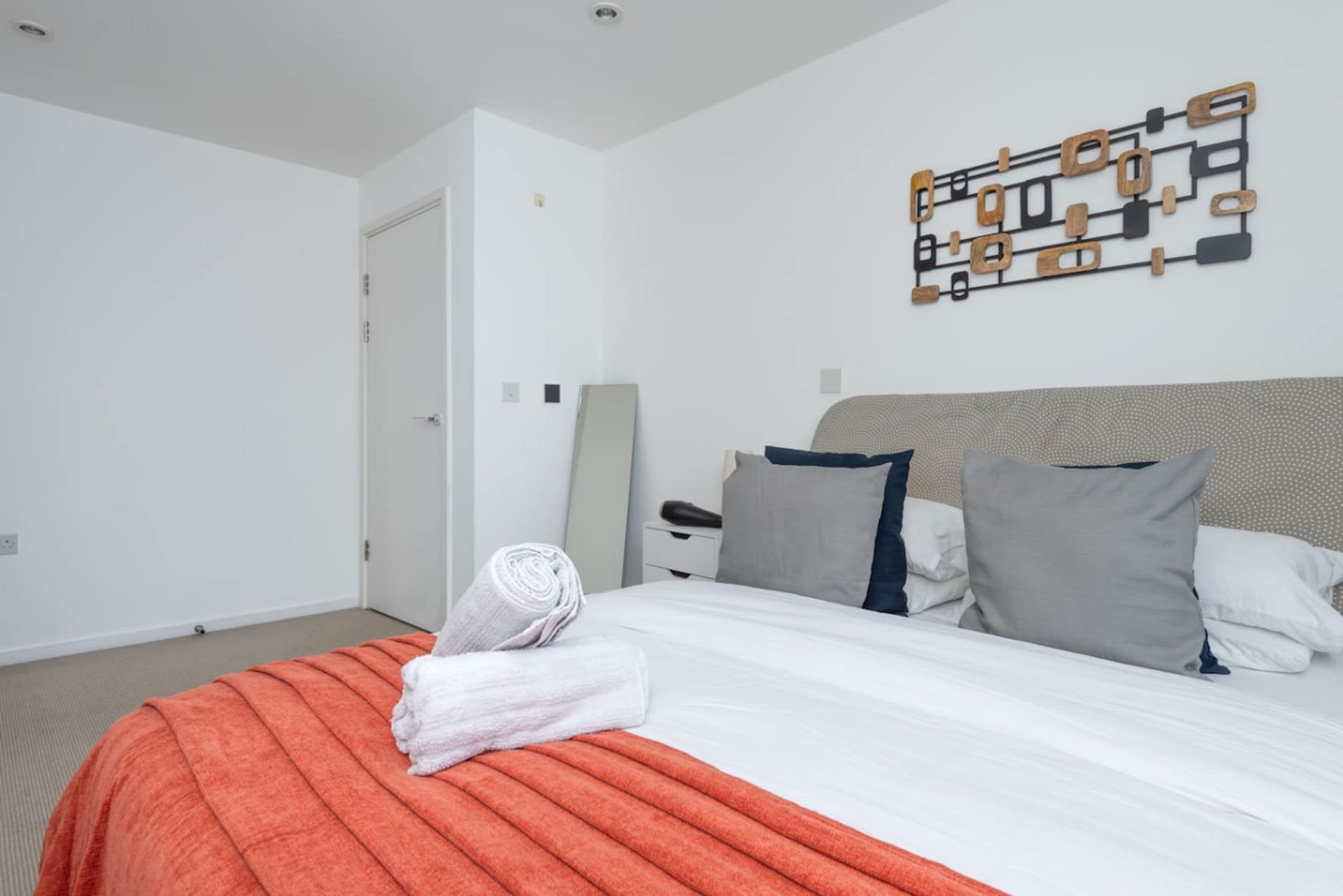 A neatly made bed with an orange blanket, a white pillow, and a grey pillow.