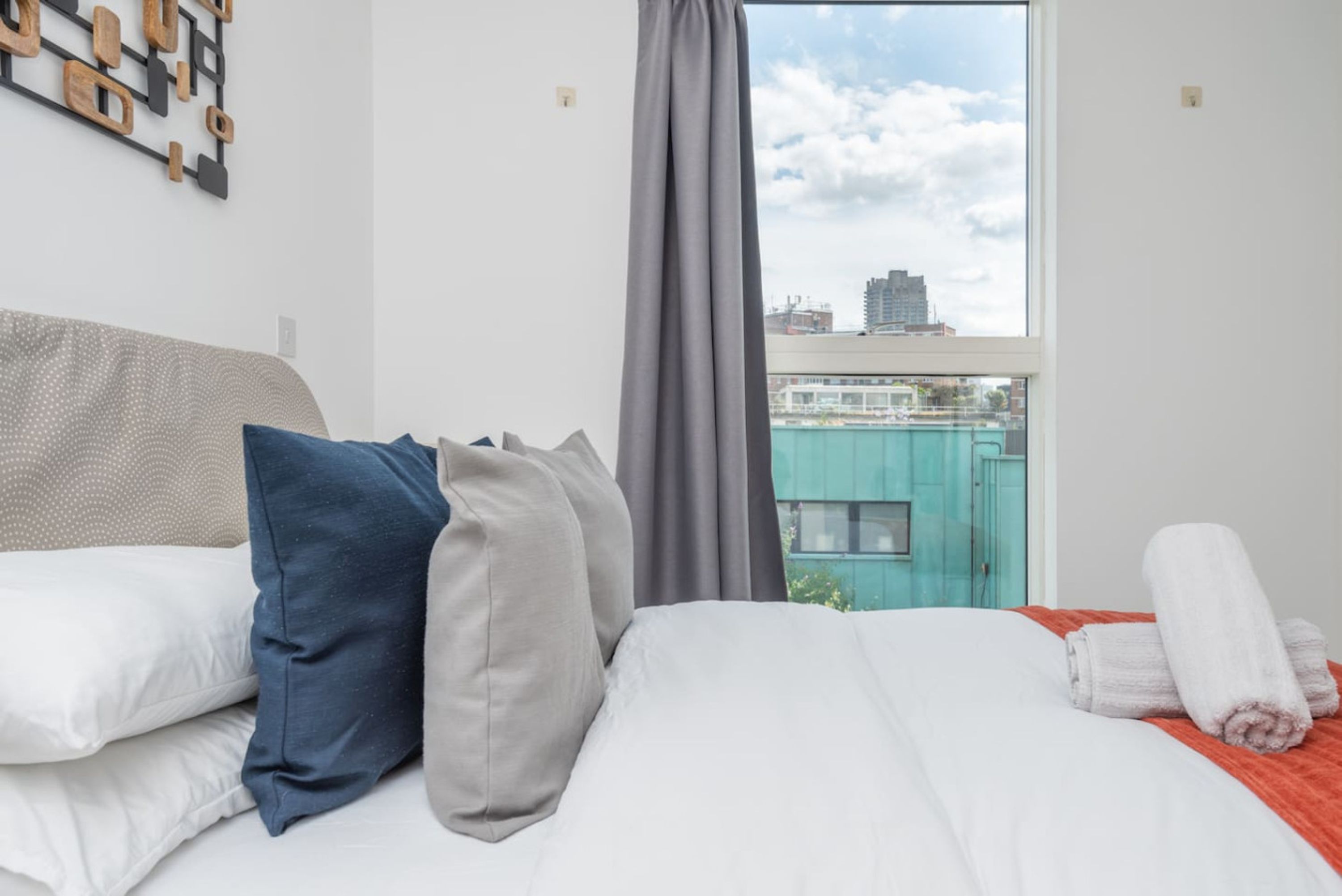A hotel room with a bed, pillows, a view of the city, and a window with curtains.