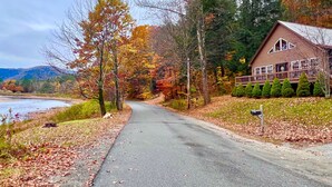 A cabin with a porch, surrounded by autumn foliage and a river. - The Perfect Adirondack Getaway Waterfront Cabin (Northville)