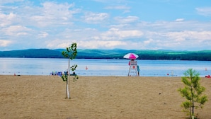 A beach with a lifeguard tower, a small tree, and a clear view of the water and distant hills. - The Perfect Adirondack Getaway Waterfront Cabin (Northville)