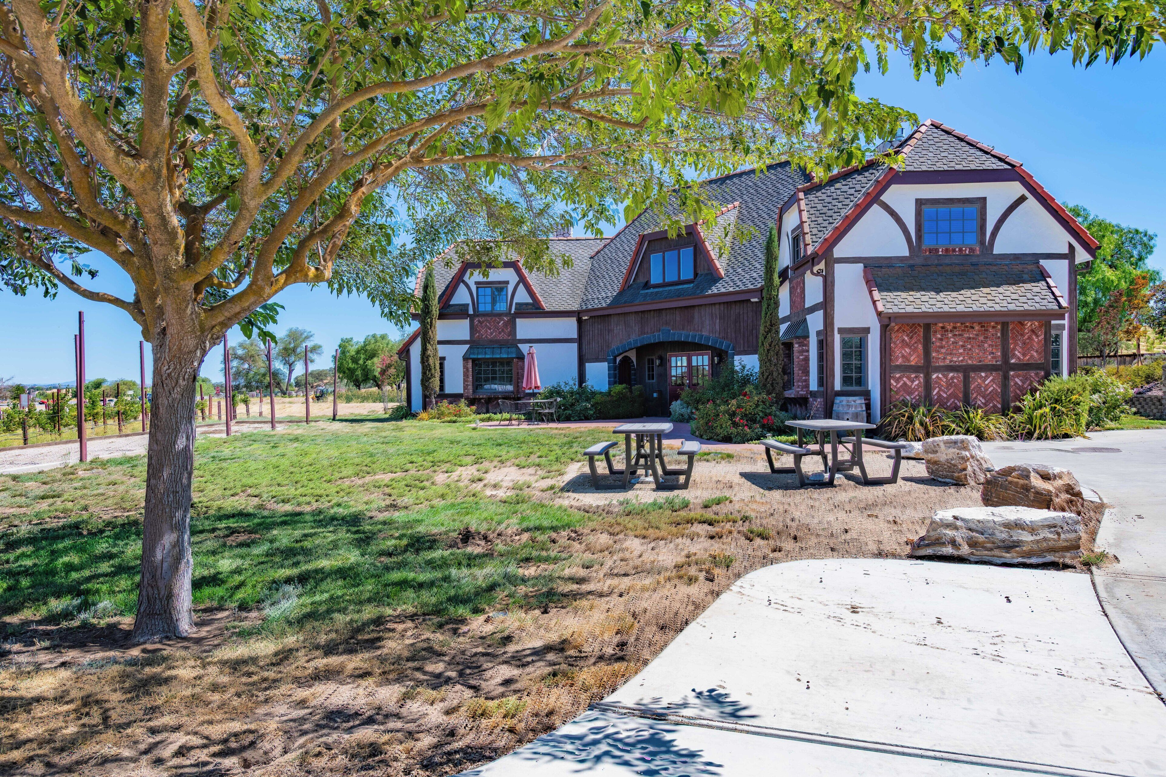 A two-story house with a large front lawn, picnic tables, and a tree.