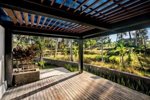 A covered outdoor area with a wooden deck, a view of a natural landscape, and a built-in planter with plants. - Villa Jehanne by BaliSuperHost (Bali)
