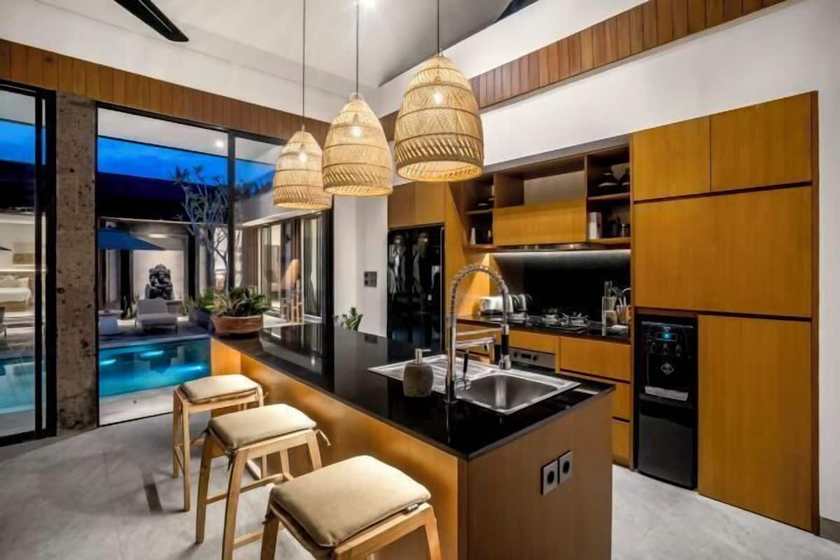A modern kitchen with a central island, wooden cabinets, and pendant lighting.