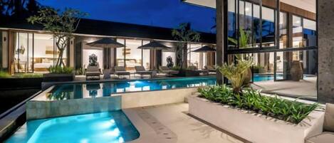 A modern outdoor pool area with lounge chairs and umbrellas, surrounded by a well-maintained garden.