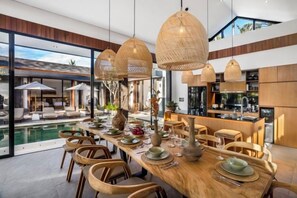 A dining area with a long table, wicker chairs, and hanging light fixtures. - Villa Jehanne by BaliSuperHost (Bali)