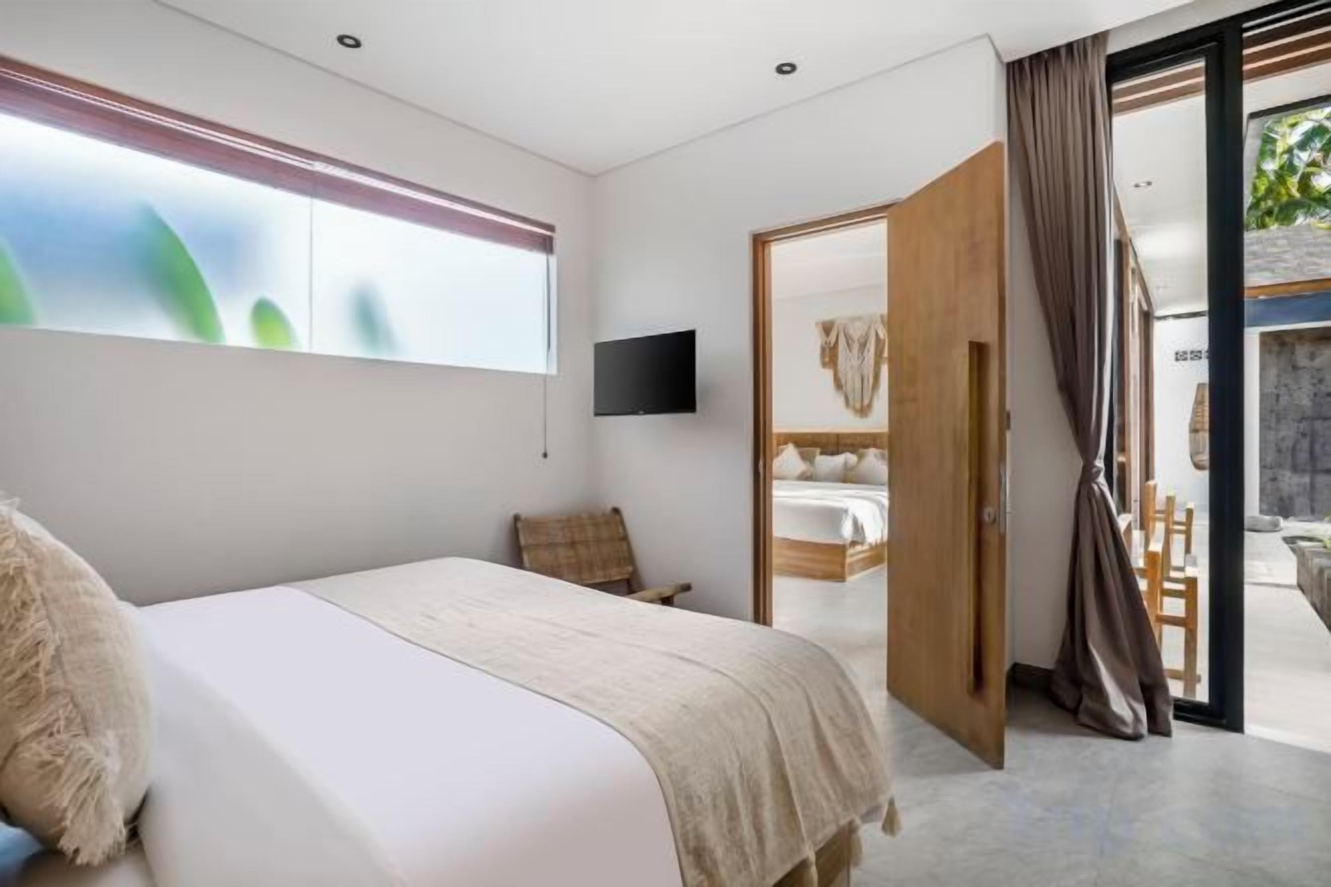 A bedroom with a bed, a television, a window, and a door leading to a balcony.