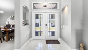 A clean, modern entryway with a double door, a chandelier, and a dog statue. - Dive into Endless Summer Bliss - Forever Summer - Roelens (Cape Coral)