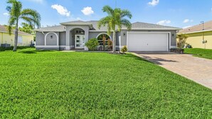 A modern two-story house with a garage, surrounded by well-maintained grass and palm trees. - Dive into Endless Summer Bliss - Forever Summer - Roelens (Cape Coral)
