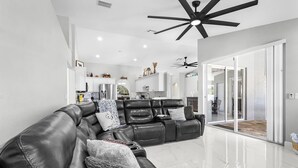A modern living room with a black leather sectional sofa, a ceiling fan, and a kitchen in the background. - Dive into Endless Summer Bliss - Forever Summer - Roelens (Cape Coral)