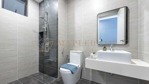 Une salle de bain moderne avec une douche à parois de verre, des toilettes blanches et un grand miroir au-dessus d’un lavabo blanc.