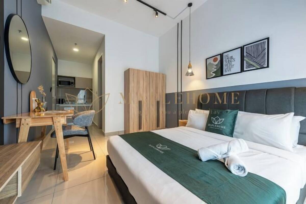 A modern hotel room with a bed, a desk, a chair, a wardrobe, and a kitchenette in the background.