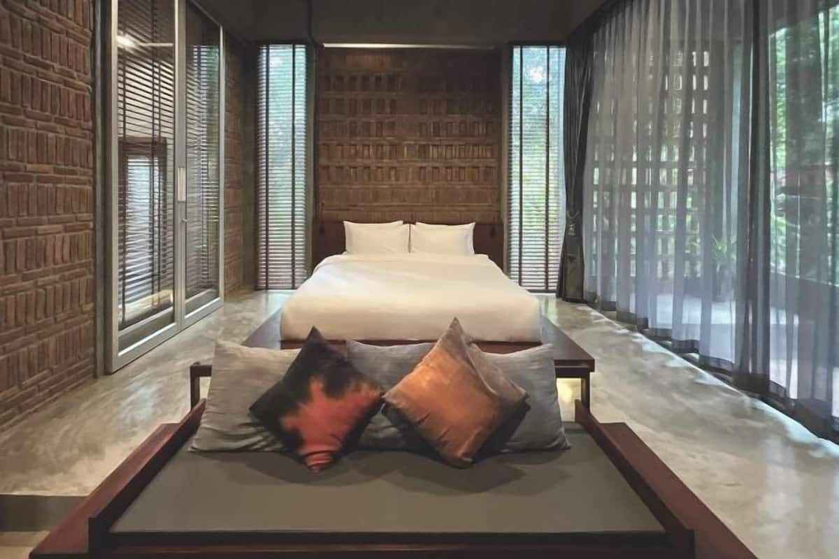 A modern bedroom with a large bed, wooden headboard, and large windows with sheer curtains.