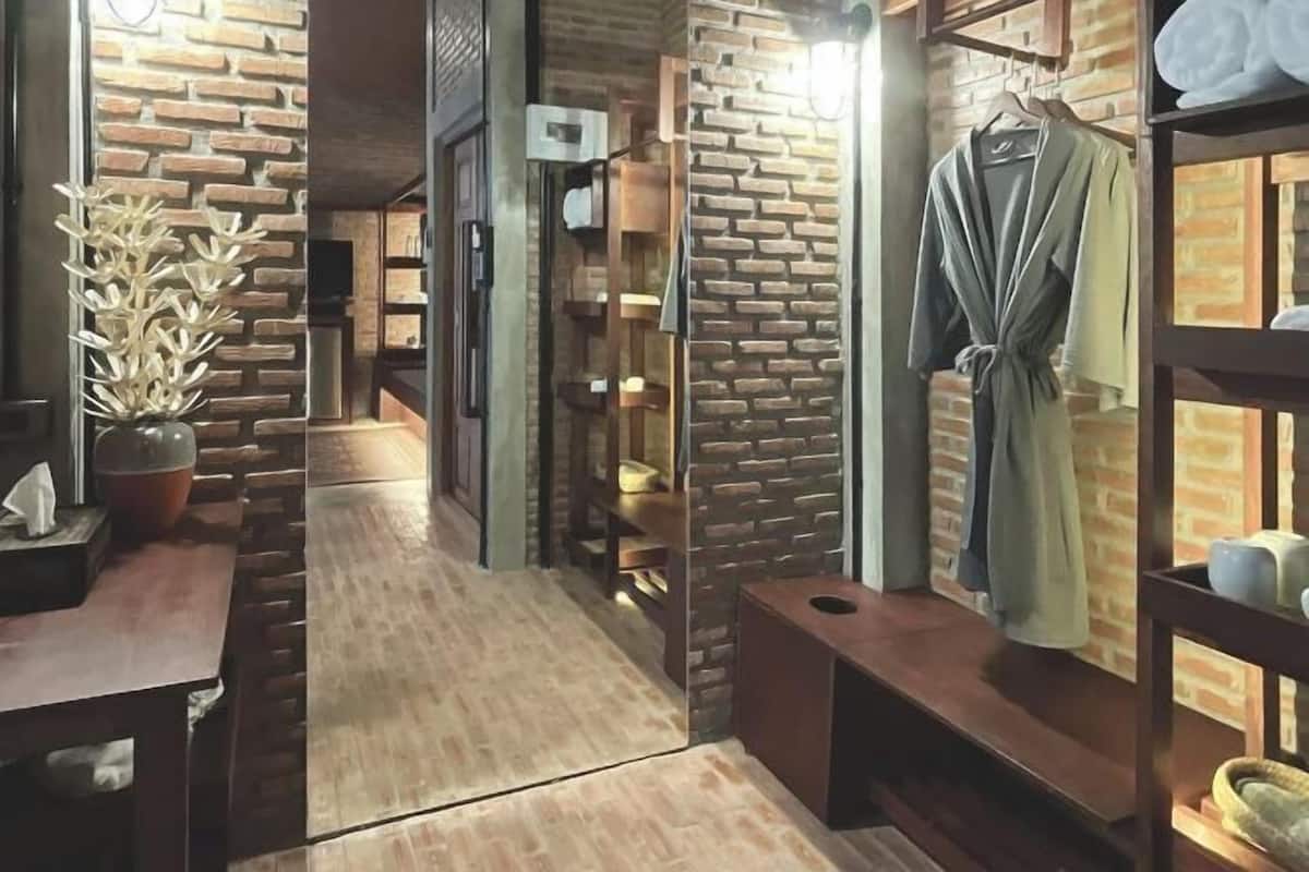 A spa room with a brick wall, wooden benches, a robe hanging, and a plant.