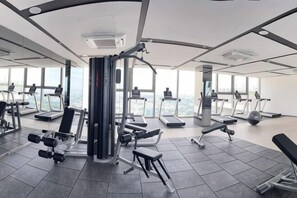 Ein Fitnessstudio mit Trainingsgeräten, Laufbändern und einem großen Fenster mit Blick auf die Stadt.