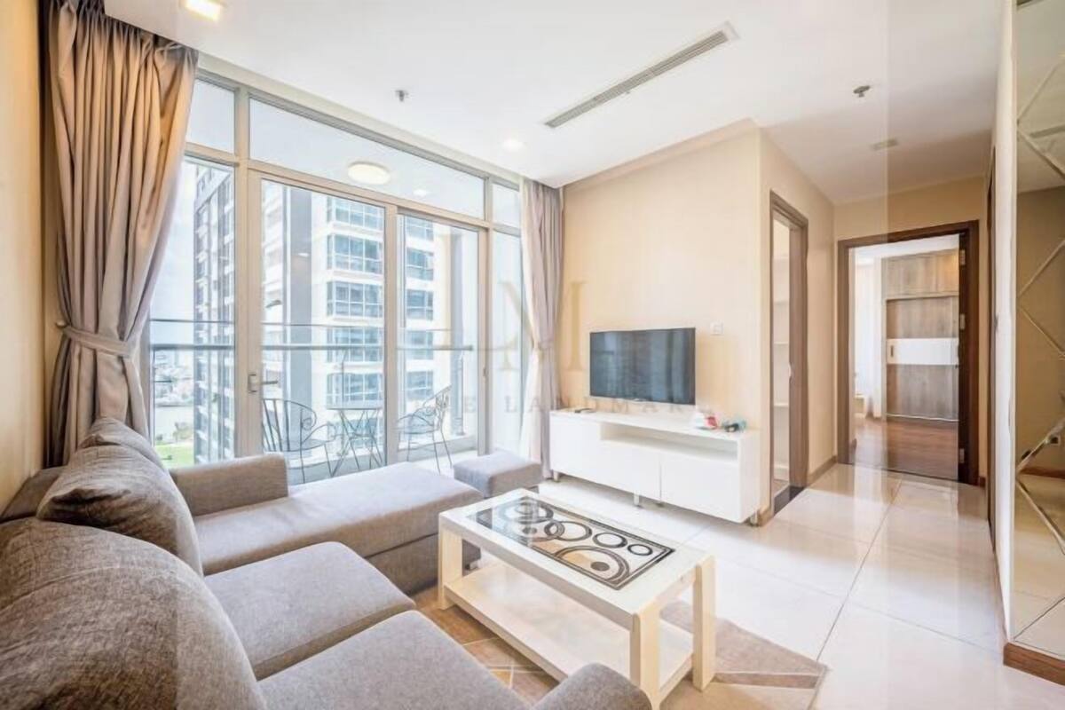 A modern living room with a sofa set, a coffee table, a TV, and a balcony with a view of buildings.