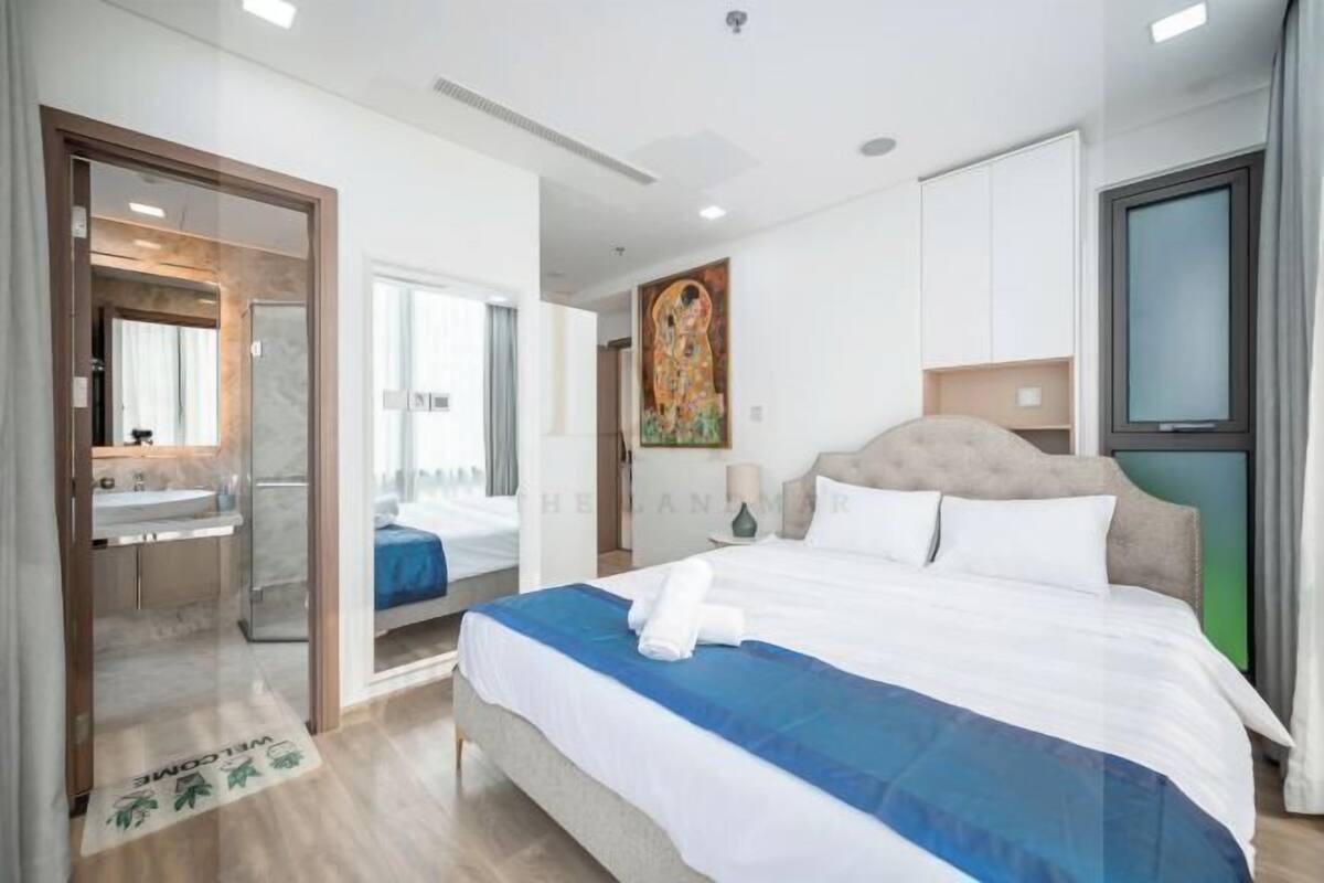 A hotel room with a bed, a painting, a TV, and a bathroom visible through an open door.