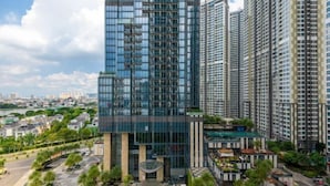A modern high-rise building with a glass facade, surrounded by a landscaped area with palm trees and a checkered pavement.
