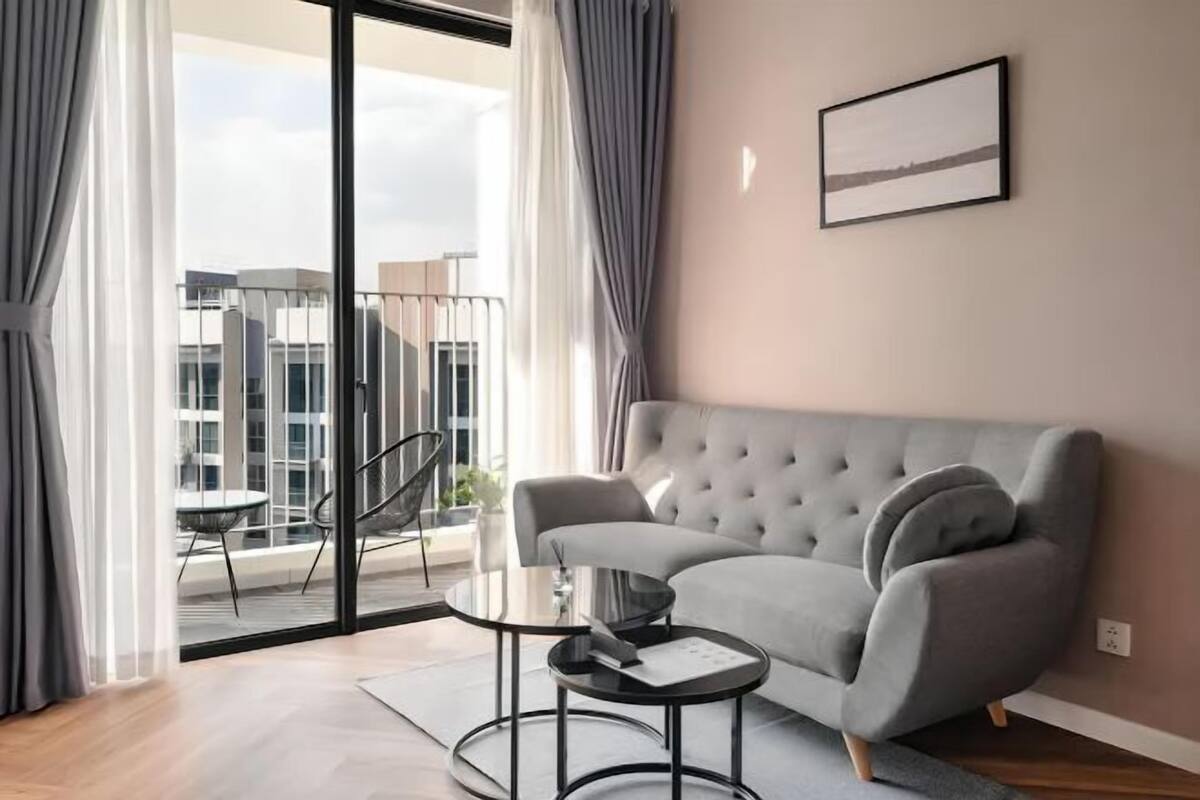 A modern living room with a grey sofa, a glass door leading to a balcony, and a framed picture on the wall.