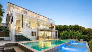 Une maison moderne à deux étages, dotée d’une piscine, d’un espace salon extérieur et d’un escalier menant à l’étage supérieur.