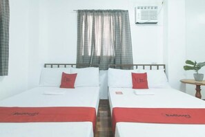 A hotel room with two single beds, a small table with a plant, and a window with curtains. - RedDoorz @ Joels Apartelle (Binan)