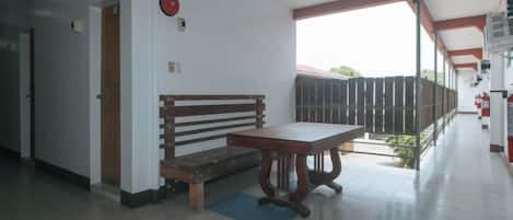 Un couloir avec un banc et une table, une porte et une vue sur l’extérieur.