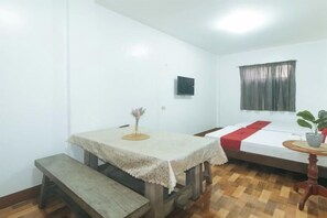 A room with a bed, a small table, a bench, and a window with curtains. - RedDoorz @ Joels Apartelle (Binan)
