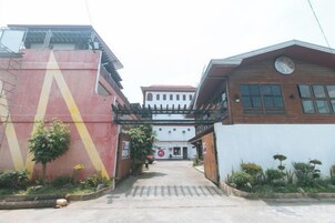 Un edificio con fachada roja y blanca, un corredor cubierto y un reloj en el lado derecho.