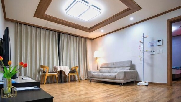 A hotel room with a wooden ceiling, a sofa, a table with chairs, a lamp, and a floor lamp. - Jungto Palace (Geoje-si)