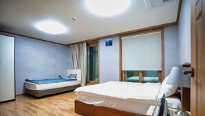 A hotel room with a bed, bedside table, lamp, and a small table with a cup. - Jungto Palace (Geoje-si)