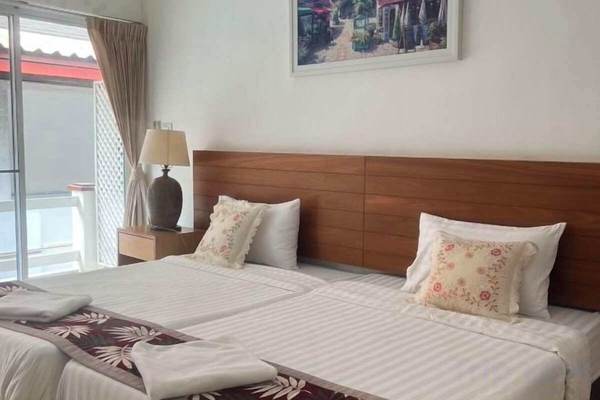 A hotel room with two beds, a wooden headboard, a nightstand with a lamp, and a painting on the wall.