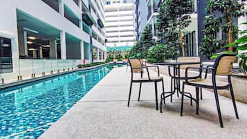 A poolside area with a table and chairs, surrounded by high-rise buildings and greenery.