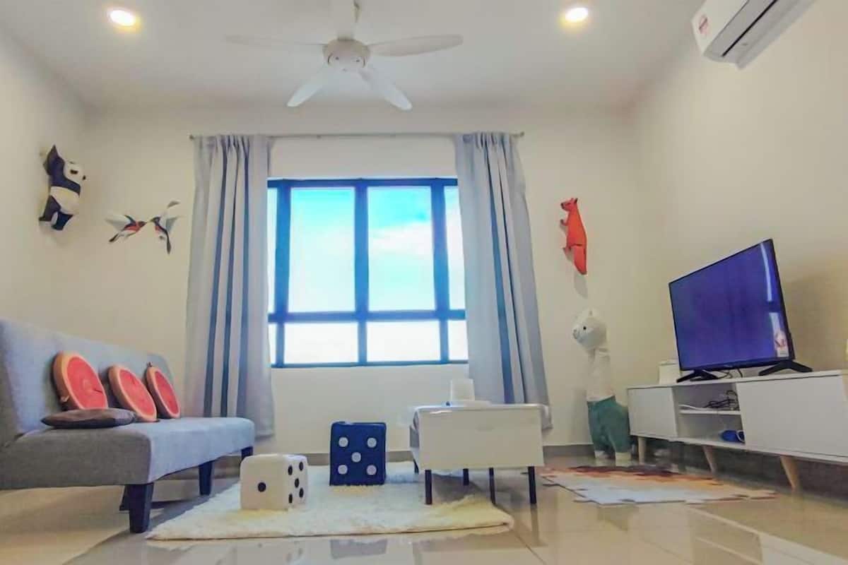 A living room with a sofa, a TV, a ceiling fan, and a window with curtains.