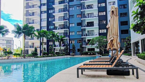Une piscine entourée de chaises longues et de parasols, le tout bordé d’un bâtiment moderne doté de balcons.
