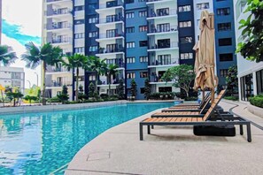 A swimming pool with lounge chairs and umbrellas, surrounded by a modern building with balconies. - Fluffy Stay at Huni Setia Alam by HCK (Shah Alam)